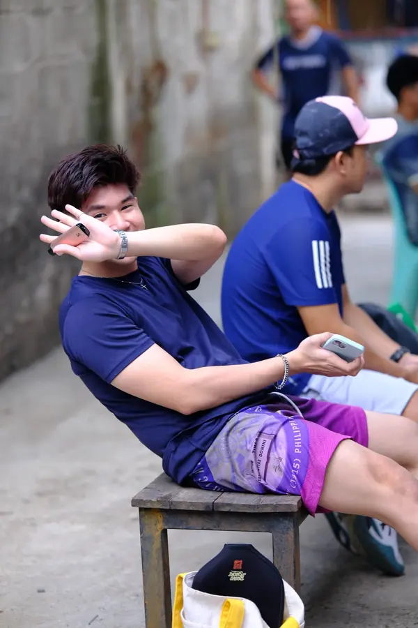 A young man in a navy shirt playfully covering his face with his hand while seated on a bench with teammates