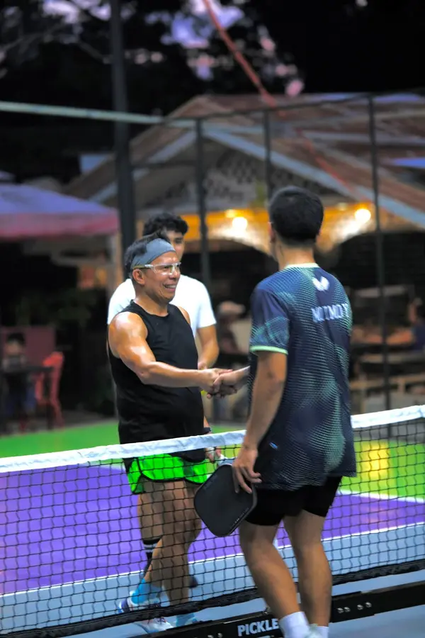 Two players shaking hands across the net after a match at RC Rally Hub in the evening