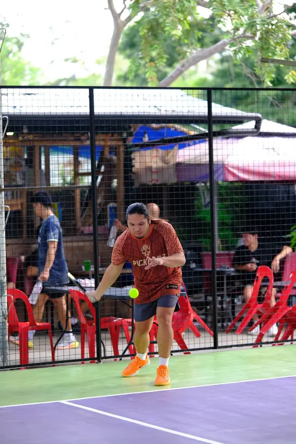 A man in an orange Pickltgz jersey reaching for a low forehand shot on the court at RC Rally Hub