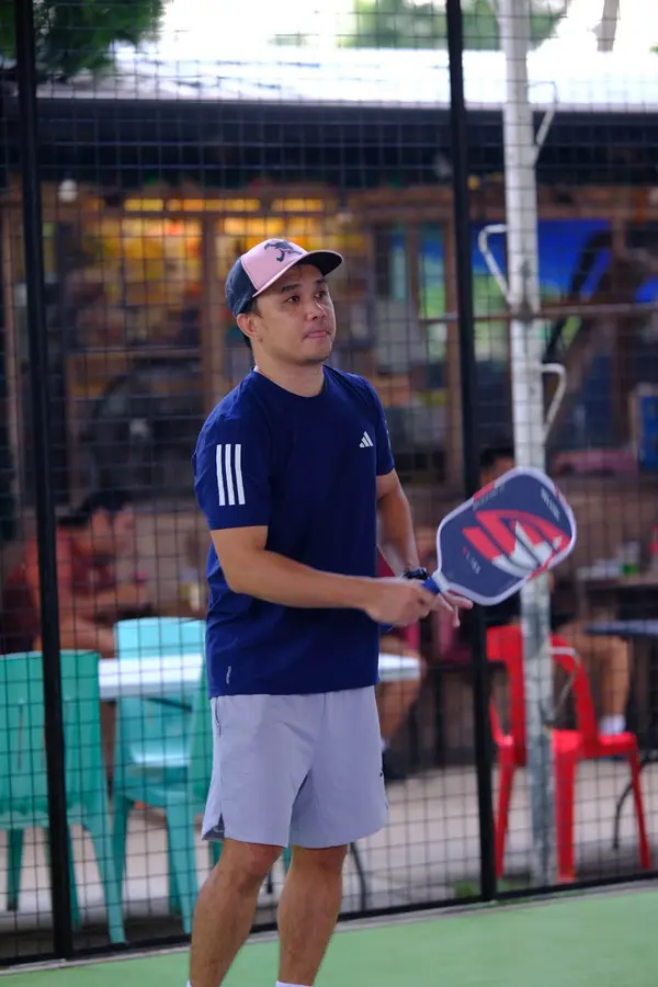 A man in a navy shirt and pink cap holding a paddle in ready position on the court