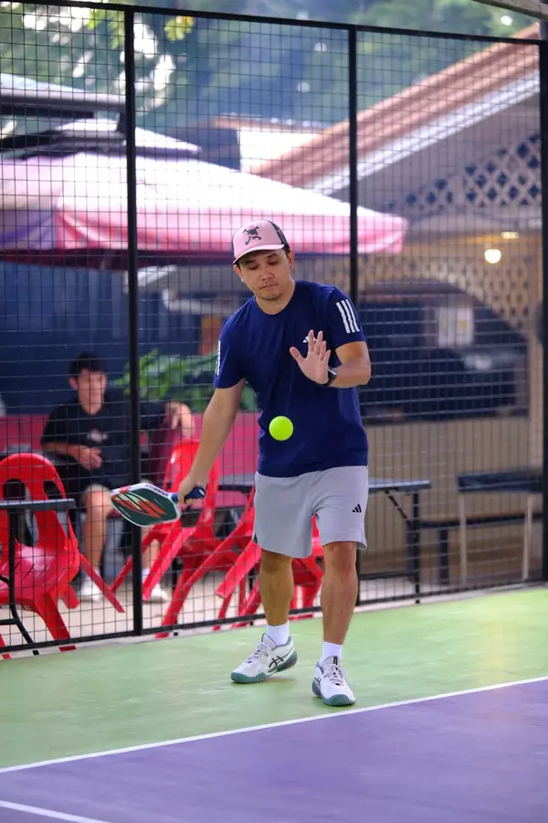 A man in a navy shirt and pink cap bouncing the ball before a serve on the court at RC Rally Hub