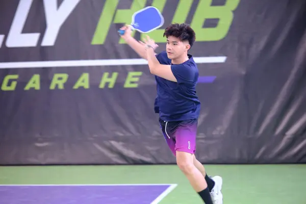 A man in a navy shirt and purple shorts following through on a forehand shot, RC Rally Hub by Garahe banner in the background