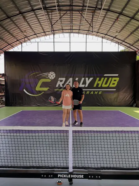 A man and woman posing together with pickleball paddles on the RC Rally Hub court