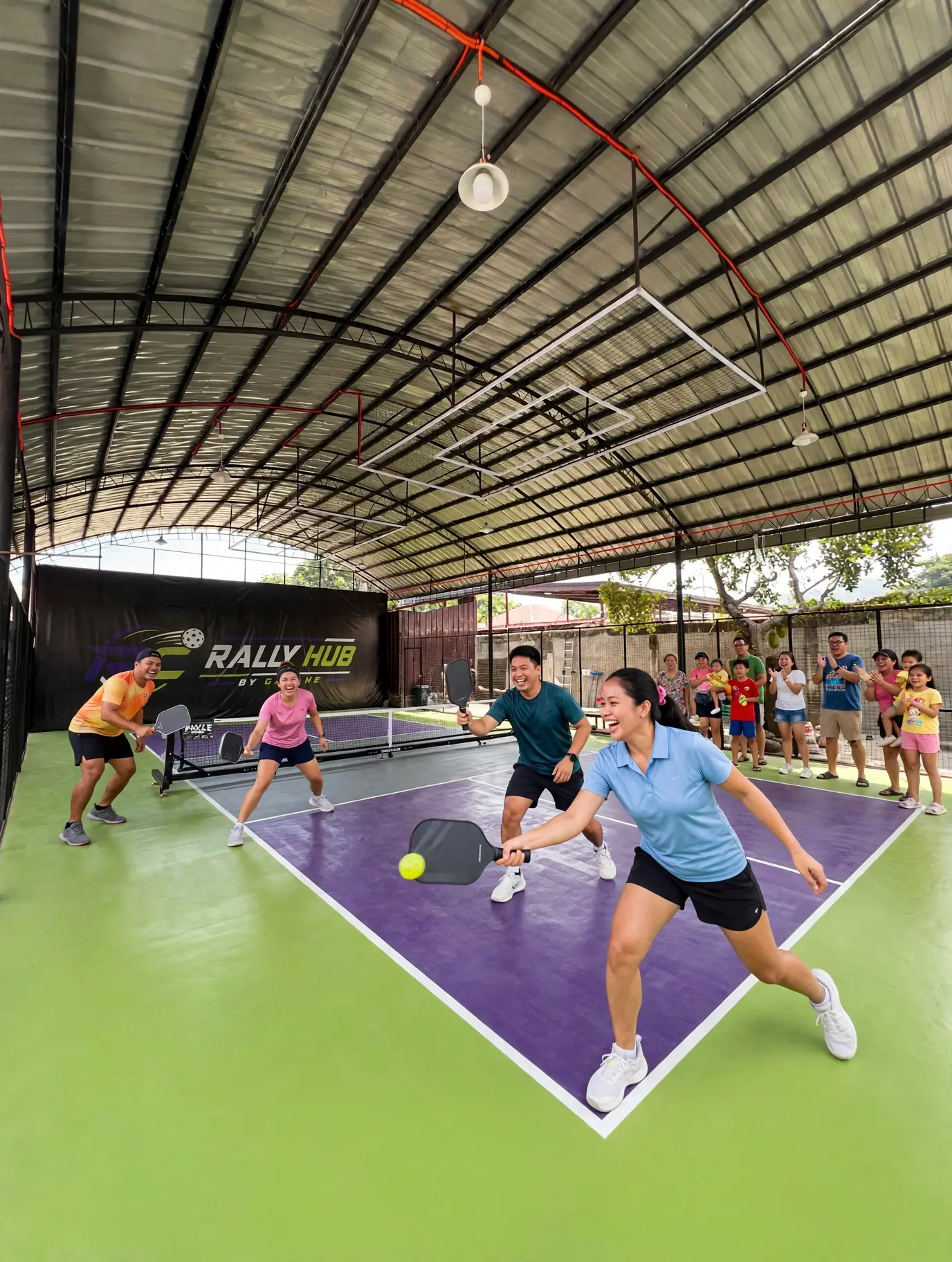 Two teams playing an energetic pickleball doubles match under the covered RC Rally Hub court, with spectators cheering courtside