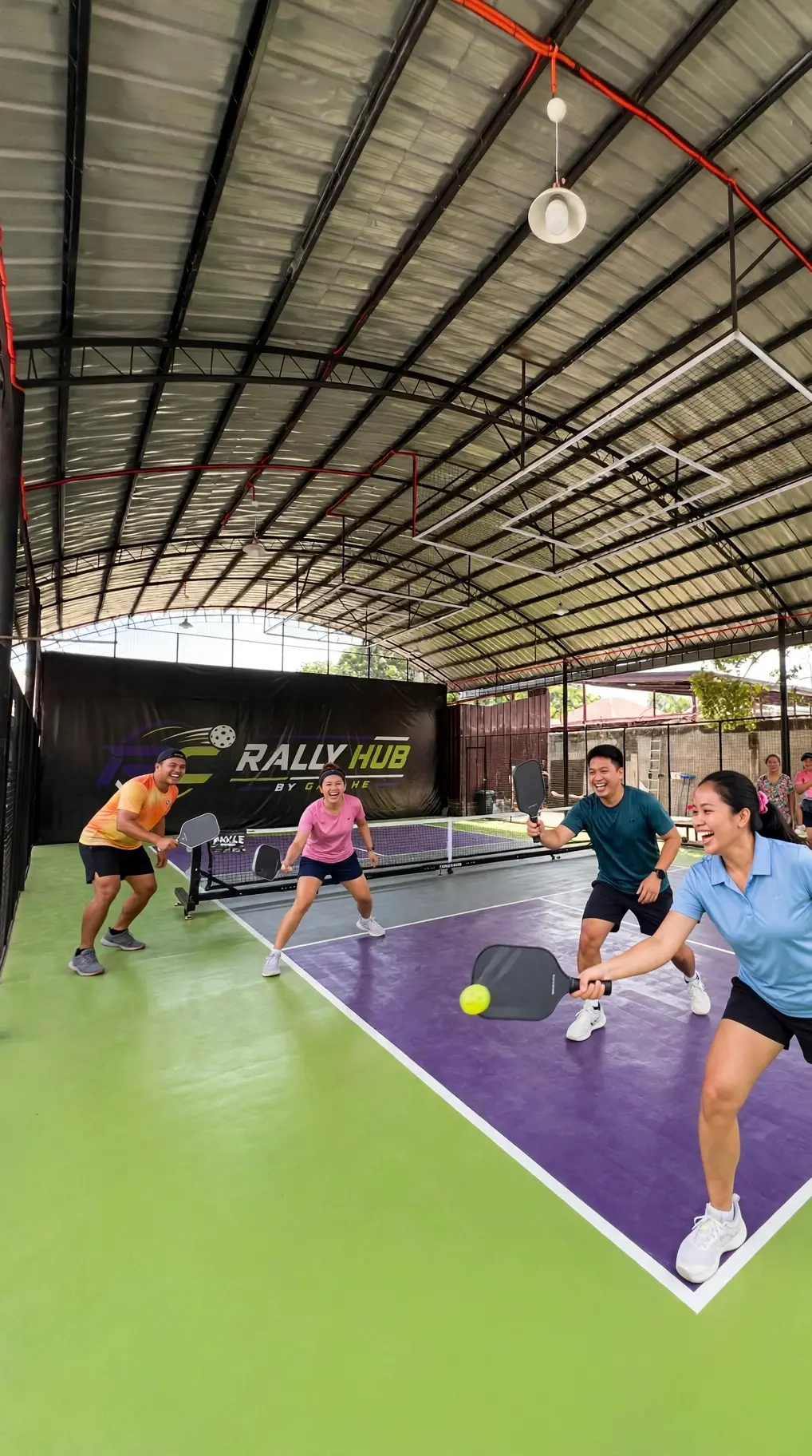 Women's doubles pickleball match at RC Rally Hub with family and friends cheering from the sidelines